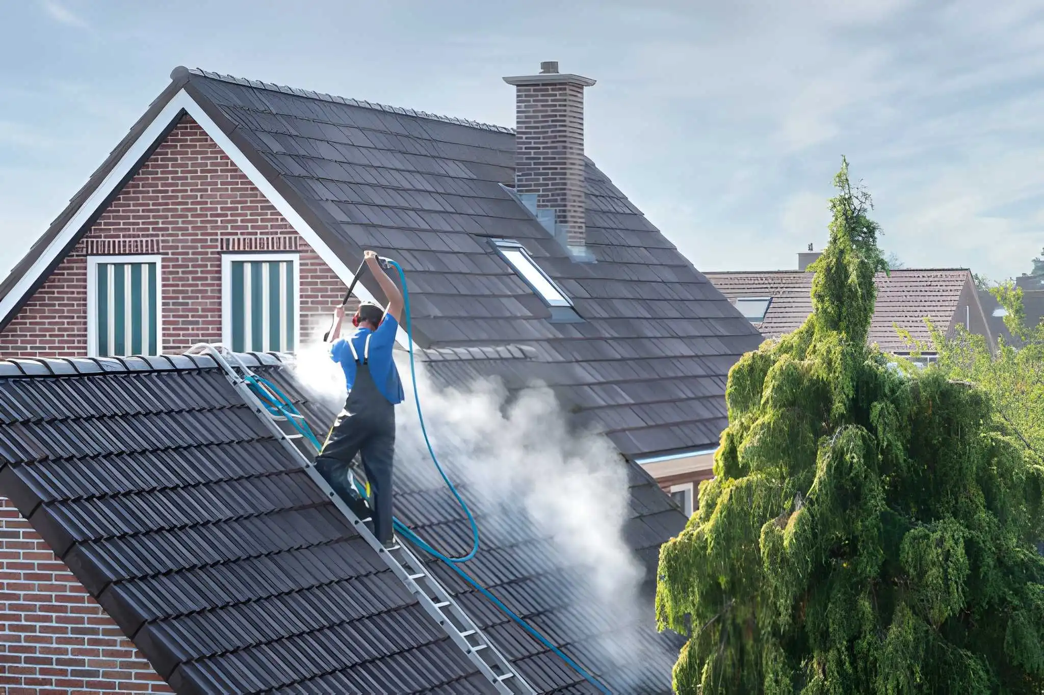 Roof pressure cleaning - Professional using pressure washer roof cleaner on red clay tile roof removing moss and algae - Roof Installation