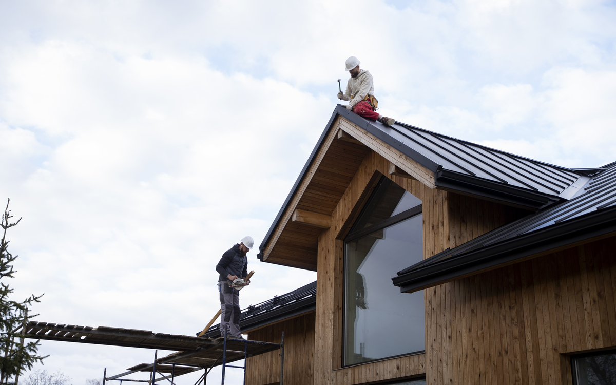 Residential roof repair attic inspection — homeowner with flashlight examining water stains on roof deck boards and daylight visible through roof sheathing in dark attic , roof repair warning signs