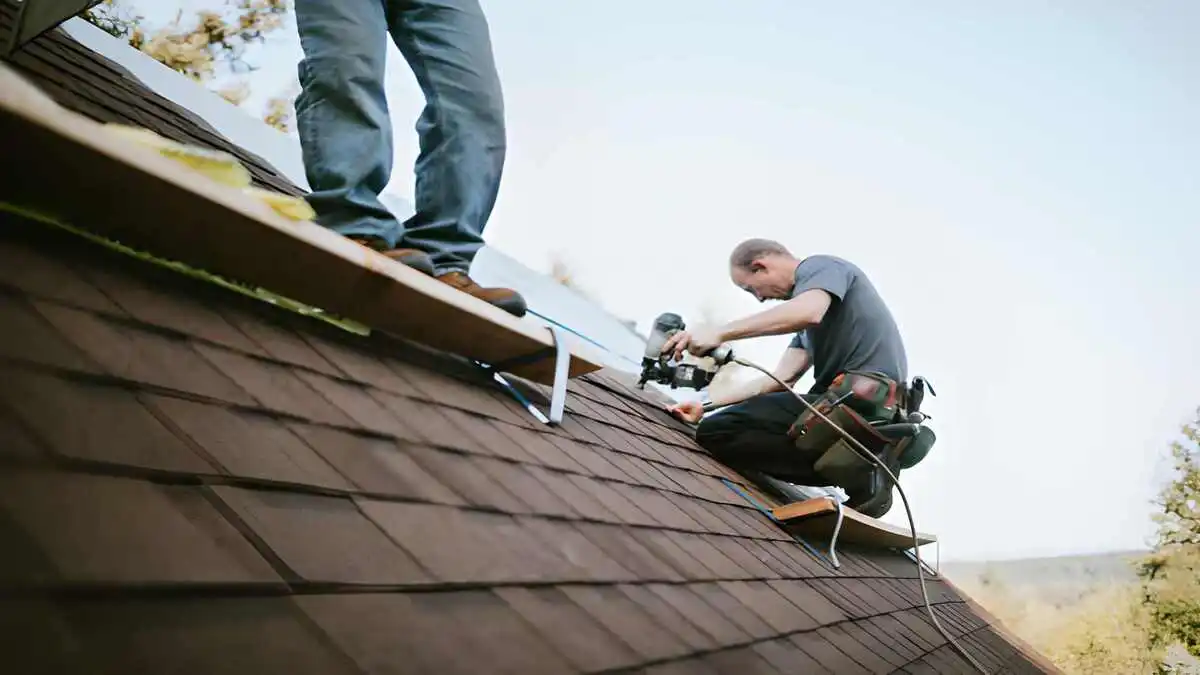 Roofing labor shortage 2026, small roofing crew of two workers installing shingles on residential home roof with visibly understaffed job site and empty scaffolding in background, contractor shortage explained