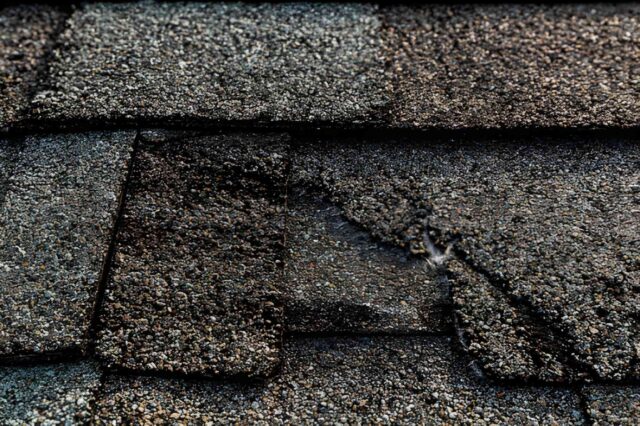 Damaged asphalt shingles curling and cracking, showing why shingles need replacement earlier than steel, affecting cost of steel roof versus shingles over time
