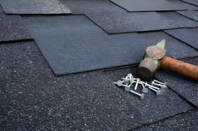 Roofer nailing asphalt shingles with a roofing hammer on a sloped rooftop